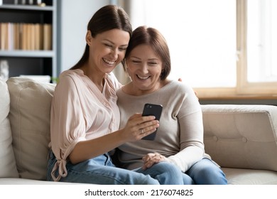 Close up happy mature mother and grownup daughter using phone together, hugging, sitting on cozy couch at home, smiling young woman embracing elderly mum, watching funny video, shopping online - Powered by Shutterstock