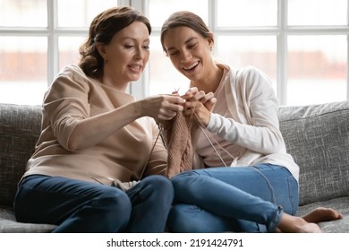 Close up happy mature mother teaching grownup daughter to knit, sitting on cozy couch at home, smiling young woman with middle aged mum enjoying leisure time, engaged in creative activity