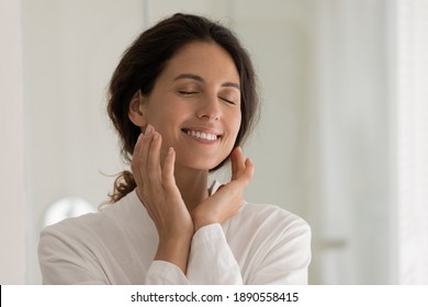 Close Up Of Happy Millennial 20s Woman In Bathrobe Touch Massage Healthy Facial Skin After Beauty Procedures. Smiling Young Lady In Home Bathroom Enjoy Glowing Face Skin After Body Care Or Treatment.