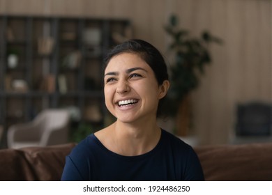 Close up of happy millennial Indian woman relax at home feel optimistic overjoyed. Smiling mixed race ethnicity female laugh look in distance visualizing or dreaming of future opportunities.