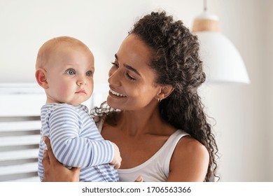 Close up of happy mother holding baby boy at home. Mixed race mother rocking adopted infant at home. Beautiful young african woman carrying adorable little child.