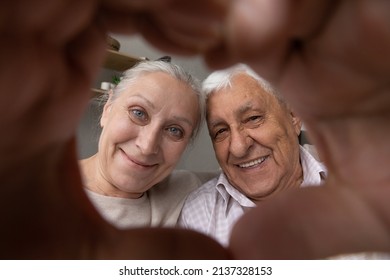 Close Up Happy Older Couple Faces, Looking At Camera Through Their Joined Fingers Showing Heart Shape, Symbol Of Affection. Express Care, Feeling Bond. I Love You, Pure Love Of Elderly Spouses Concept