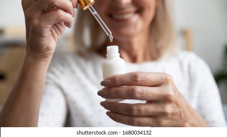 Close Up Happy Older Woman Opening Bottle With Essence, Pipetting Skincare Product. Smiling Middle Aged Lady Using Pleasant Fragrance Liquid Or Antiaging Moisturizing Oil, Beauty Procedure At Home.