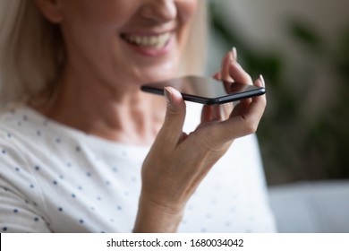 Close up happy older woman using voice recognition function or virtual assistant on mobile phone. Smiling smart middle aged lady recording voice message in social networks for friends or family.