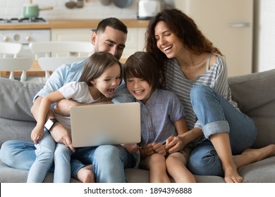Close up happy parents with daughter and son using laptop sitting on couch at home. Smiling mother, father and cute children looking at laptop screen using video call. Family having fun with computer.