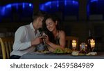 Close up of happy passionate couple in love drinking wine at romantic date and flirting. Handsome loving husband whispering on ear beautiful young wife. Dating concept