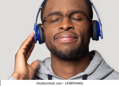 Close up of happy satisfied african American male wearing blue headphones enjoy music, calm smiling black man isolated on grey studio background listen to radio favorite tracks in earphones - Powered by Shutterstock