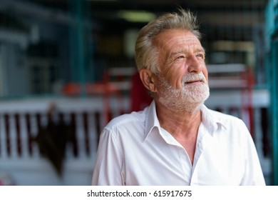 Close up of happy senior bearded man smiling while thinking and looking up outdoors - Powered by Shutterstock