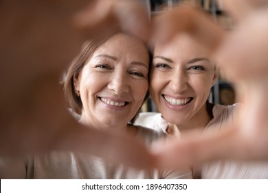 Close Up Happy Smiling Mature Mother And Grownup Daughter Taking Selfie Together, Looking Through Fingers, Making Heart Gesture With Hands, Family Enjoying Leisure Time, Having Fun With Camera,