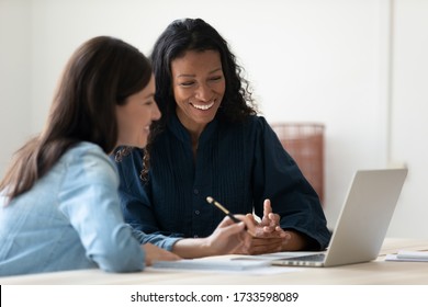 Close up happy young african american businesswoman using laptop with laughing female mentor in coworking boardroom at meeting. Smiling diverse woman managers talking about new business concept.