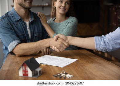 Close up of happy young Caucasian couple buyer handshake close deal buy house at realtor office. Smiling man and woman clients shake hands make agreement with real estate agent. Rent concept.