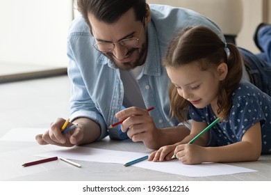 Close up of happy young Caucasian father and little daughter have fun enjoy drawing in album together. Smiling caring dad and small girl child involved in painting at home. Art, hobby concept.
