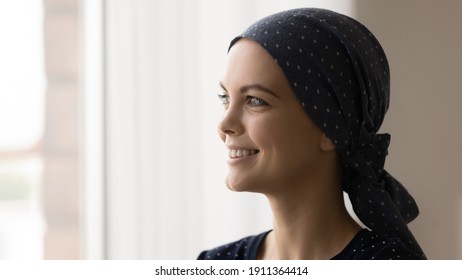 Close Up Of Happy Young Caucasian Female Cancer Patient With Scarf On Head Look In Window Distance Dream Of Remission. Smiling Woman Struggle With Oncology Hope For Recovery Or Good Treatment Results.