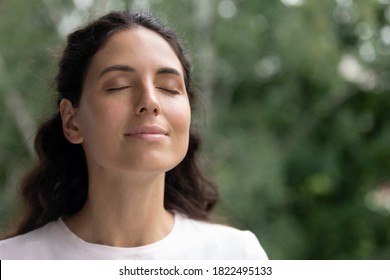 Close up of happy young Caucasian woman isolated on blurred background dream visualize with eyes closed. Smiling dreamy female breathe fresh air relieve negative emotions. Stress free concept.