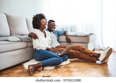 Close Up Of A Happy Young Couple Using Laptop At Home. Young Couple Enjoying Lazy Sunday Using Laptop By The Window. Happy Couple Using Laptop Sitting On Floor Indoor