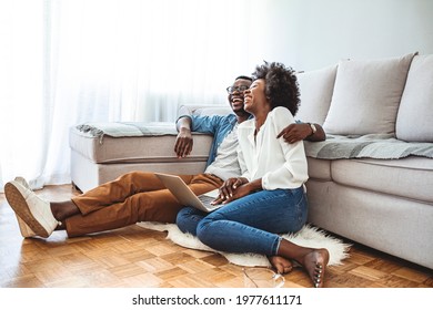 Close Up Of A Happy Young Couple Using Laptop At Home. Young Couple Enjoying Lazy Sunday Using Laptop By The Window. Happy Couple Using Laptop Sitting On Floor Indoor