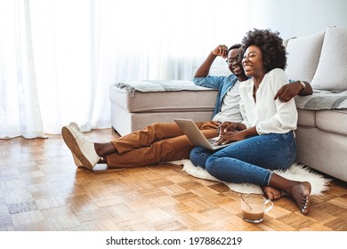 Close Up Of A Happy Young Couple Using Laptop At Home. Young Couple Enjoying Lazy Sunday Using Laptop By The Window. Happy Couple Using Laptop Sitting On Floor Indoor