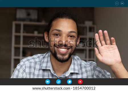 Close up happy young handsome african ethnicity man employee waving hand, welcoming colleagues teammates at online distant meeting, using computer software video call application, working from home.
