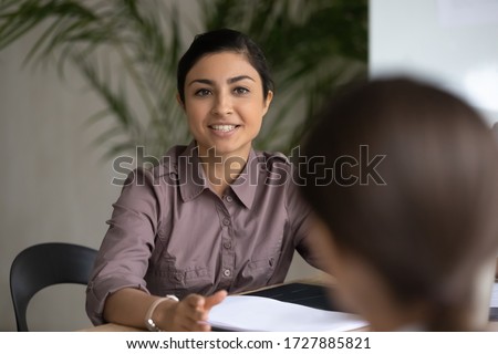Close up happy young indian ethnic businesswoman talking about finance business project. Smiling diverse attractive female leader discussing sales presentation with workers in boardroom at meeting.
