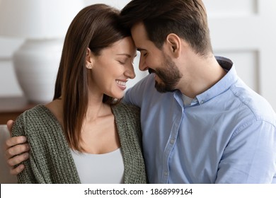 Close up of happy young man and woman lovers touch foreheads enjoy tender intimate moment together. Smiling Caucasian couple feel romantic at home hug embrace show love and care in relationship.