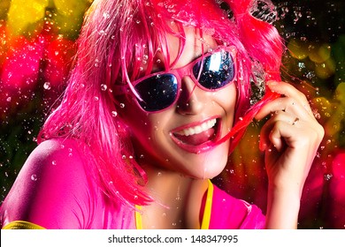 Close up Happy Young Party Girl Wearing Dark Pink Wig, Shades and Shirt on a Water Splash, with Toothy Smile Expressing Happiness.