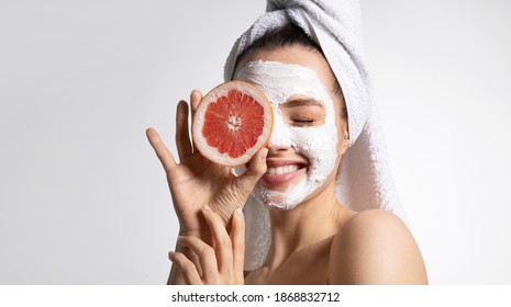 Close up of happy young playful teen girl in moisturizing mask and towel holds grapefruit covers eye. Advertising poster of facial eco-friendly skincare products. Morning beauty routine - Shutterstock ID 1868832712