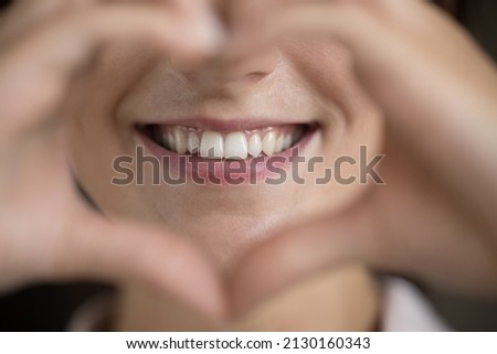 Close up happy young woman making heart sign, showing straight white teeth, feeling with professional dental services. Thankful millennial female client demonstrating healthy teeth, oral care concept.