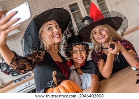 Close up of happy young woman mother witch taking selfie photo video call on smart phone and having fun with her kids in Halloween decorated kitchen