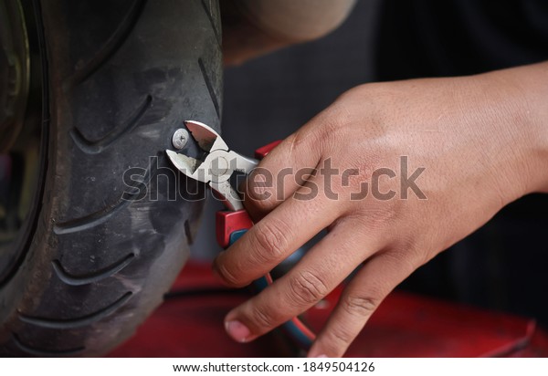 Close up he mechanic\'s hand was tugging the nail\
from the motorcycle tire.