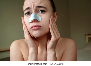 Close up head shot attractive lady with cleansing strip on nose looking at camera. Photo of upset woman  squeezing pimple on her face . Sad, surprised female face.