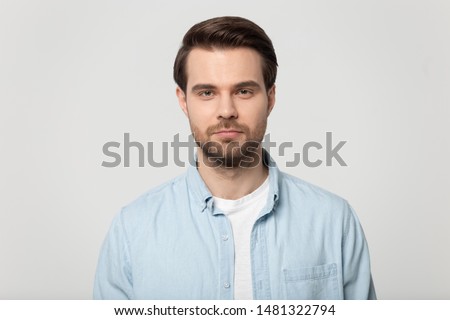 Close up head shot confident serious concentrated young man looking at camera studio portrait, isolated on grey white studio background. Thoughtful millennial guy posing for album photo.