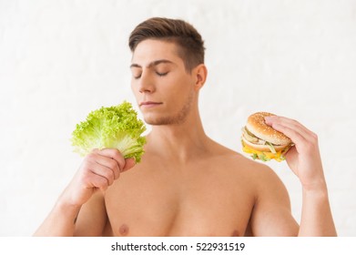 Close Up Head Shot Of A Man Smelling Salad And Holding Burger In Other Hand Isolated On White Background