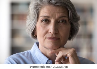 Close up head shot portrait of beautiful thoughtful pleasant older senior woman touching chin looking at camera, mature attractive elderly mature grandmother holding video call, pose at home. - Powered by Shutterstock