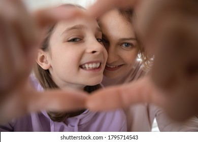 Close up head shot portrait happy mother and teenage daughter making heart gesture, looking through fingers at camera, overjoyed mum and smiling teenager girl showing love sign, posing for photo