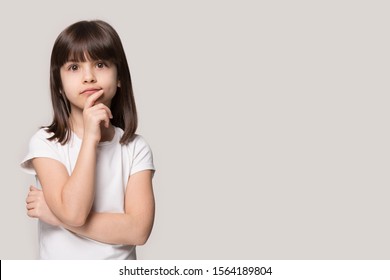 Close up head shot portrait image with thoughtful little girl. Concept kid having dilemma and thinking about trouble on gray background, six year child looking at camera with hand on chin, copy space