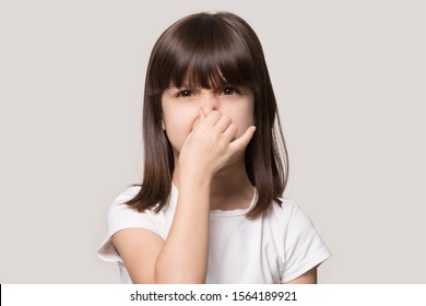 Close Up Head Shot Portrait Image With Shocked Little Girl. Concept Unhappy Kid Feeling Bad And Dislike Smell And Hold Nose From Funny Odor, Stinky On Gray Background, Six Year Child Looking At Camera