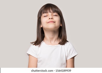 Close up head shot portrait image with relaxed little brown-haired girl, reduce stress. Wellbeing concept rest kid meditating and deep breathing on gray background, six year child with eyes closed