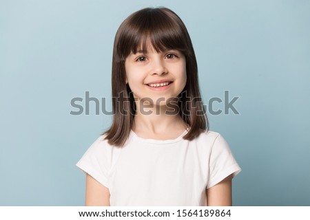 Close up head shot portrait image with smiling little brown-haired girl. Concept happy and beauty kid with good healthy teeth for dental on blue background, six year child looking at camera and posing