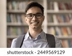 Close up head shot portrait of Indian student guy with backpack pose standing in campus library on bookshelves background. University education, professional skills, gain new knowledge, studentship