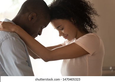 Close up head shot side view tender happy african american woman cuddling smiling beloved husband neck, touching foreheads with closed eyes, feeling love, sincere feelings, enjoying caress moment.