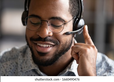 Close up head shot smiling friendly african american professional technical support manager in eyeglasses call center operator assistant wearing headset with mic answering consulting clients.