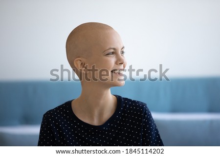 Close up head shot smiling hairless woman suffering from oncology looking to aside, dreaming about good future, visualizing, optimistic young female patient with oncology sitting on bed