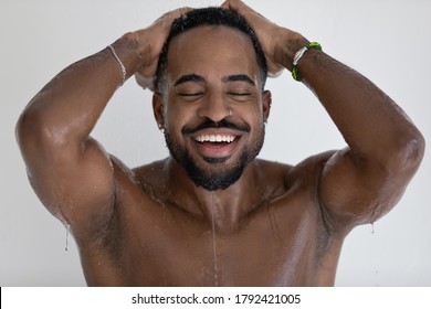 Close up head shot smiling overjoyed African American handsome young man with closed eyes taking shower, washing head, standing in bathroom, enjoying morning routine procedure, relaxing