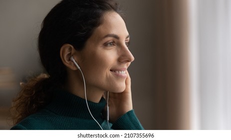 Close up head shot young attractive woman listening favorite popular music in wired earphones, looking in distance, daydreaming or enjoying peaceful calm weekend pastime alone at home, hobby activity. - Shutterstock ID 2107355696