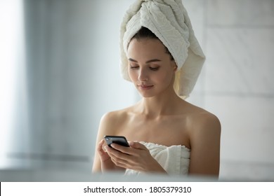 Close up head shot young woman wearing white bath towel on head using smartphone, beautiful female standing in bathroom, chatting in social network, texting online after morning shower - Powered by Shutterstock