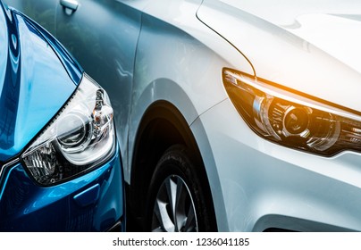 Close Up Headlamp Light Of Blue And White SUV Car. Blue Car Parked Beside White Car. Automotive Industry Concept. Electric Or Hybrid Auto Concept. Car Service. Road Trip Adventure. Automobile Rental.