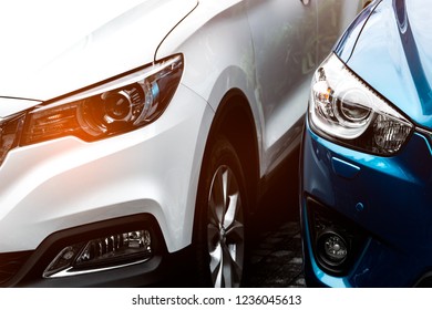 Close up headlamp light of blue and white SUV car parked on concrete parking lot of the hotel or shopping mall. Automotive industry concept. Electric or hybrid car technology. Car rental concept.
