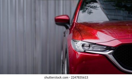 close up headlight of red car against gray blurred background.