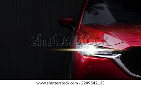 close up headlight of red car against black background.