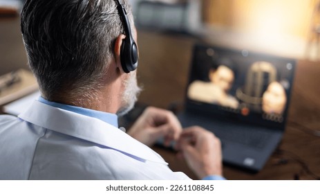 Close up headset. Back view. Senior caucasian doctor online video call conference with headset consult patient on laptop computer. Doctor online consultation and telehealth medicine - Shutterstock ID 2261108845